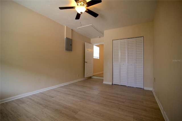 unfurnished bedroom featuring wood finished floors, baseboards, attic access, electric panel, and a closet