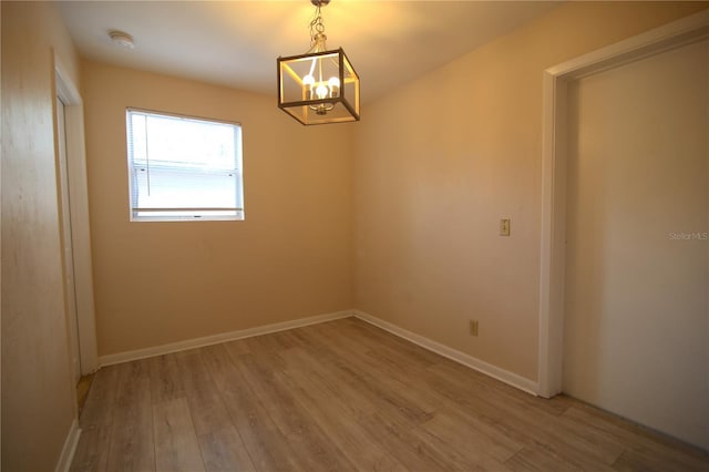 empty room with a chandelier, baseboards, and wood finished floors