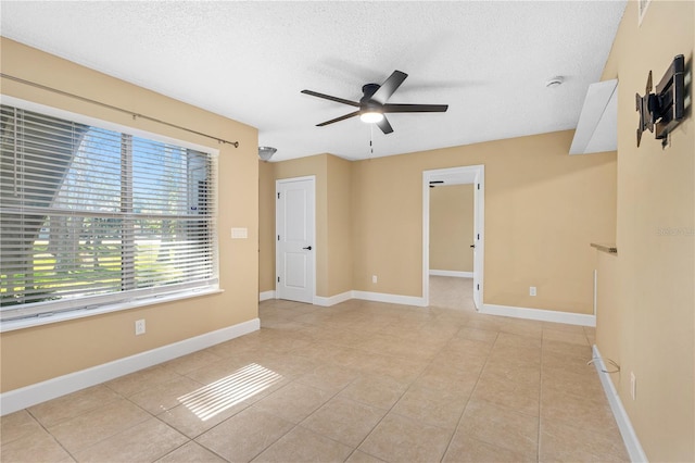 spare room with ceiling fan, light tile patterned floors, baseboards, and a textured ceiling