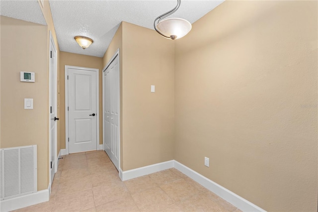 hall featuring visible vents, baseboards, a textured ceiling, and light tile patterned flooring