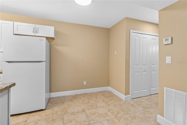 kitchen with visible vents, freestanding refrigerator, white cabinets, light tile patterned floors, and baseboards