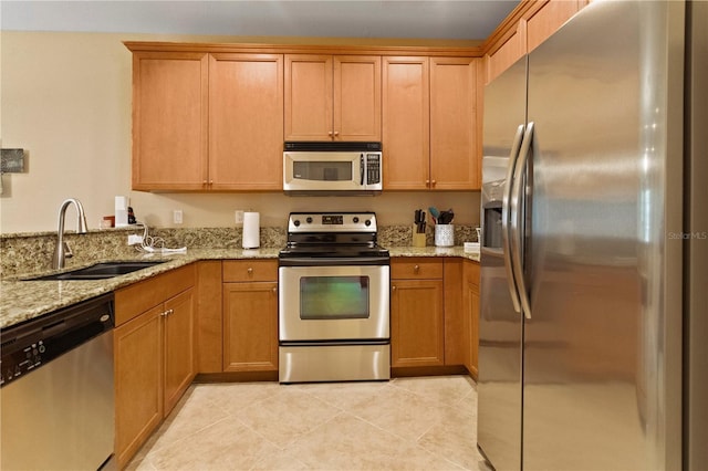 kitchen with light stone countertops, light tile patterned floors, brown cabinetry, stainless steel appliances, and a sink