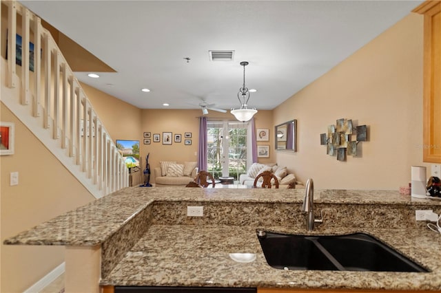 kitchen featuring visible vents, light stone countertops, open floor plan, and a sink