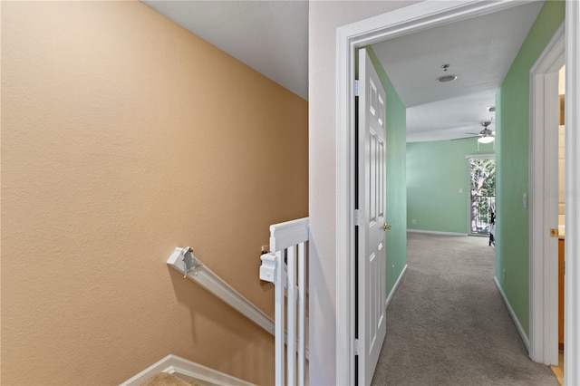 corridor featuring baseboards, an upstairs landing, and carpet flooring