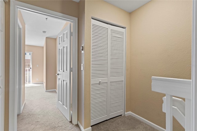 hall featuring a textured wall, baseboards, and light carpet