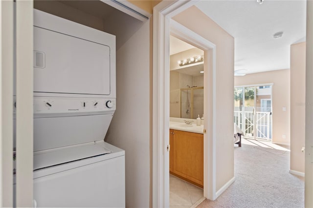 laundry area featuring baseboards, light colored carpet, stacked washer and dryer, laundry area, and a sink