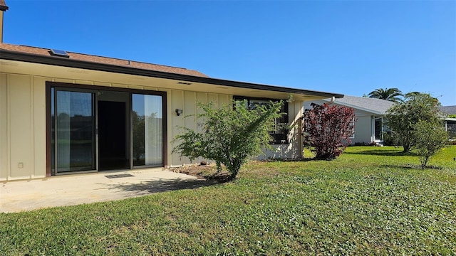 rear view of property with board and batten siding, a yard, and a patio