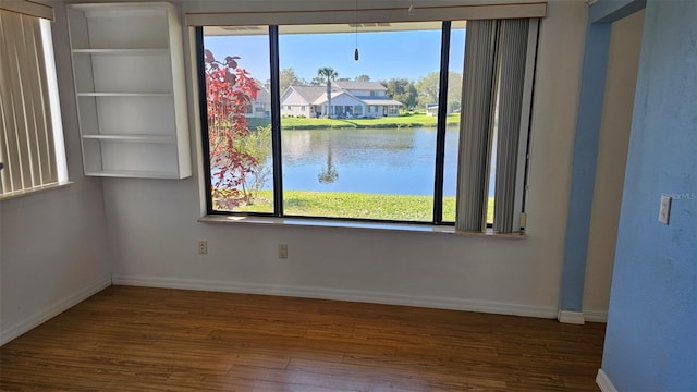 spare room featuring baseboards, a water view, and wood finished floors