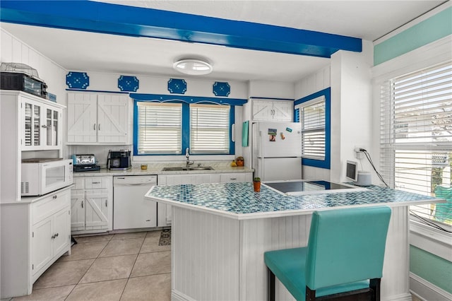 kitchen with a kitchen bar, light tile patterned flooring, white appliances, white cabinetry, and a sink