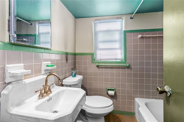 bathroom with toilet, tile walls, plenty of natural light, and a sink