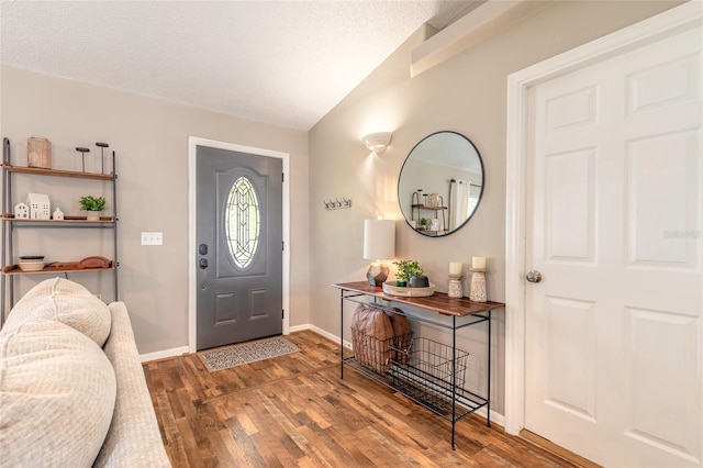 entryway with vaulted ceiling, wood finished floors, baseboards, and a textured ceiling