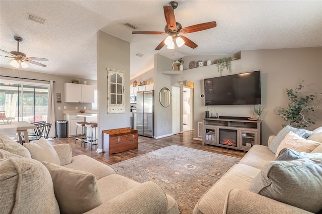 living room with a ceiling fan, vaulted ceiling, wood finished floors, and visible vents