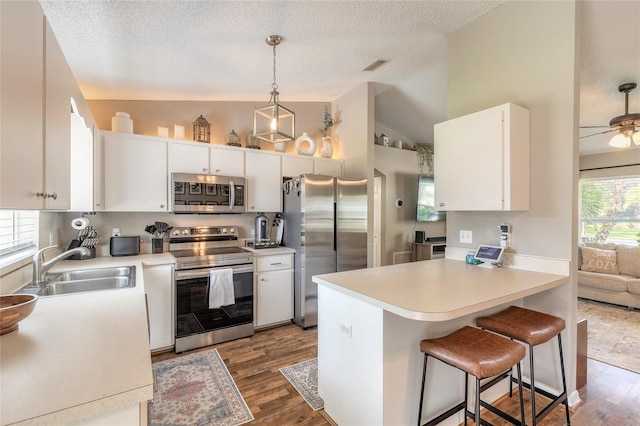 kitchen featuring visible vents, a sink, stainless steel appliances, a peninsula, and lofted ceiling