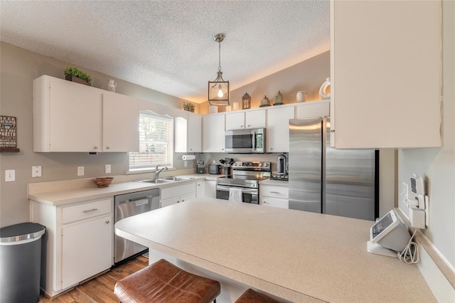 kitchen featuring lofted ceiling, a peninsula, a sink, light countertops, and appliances with stainless steel finishes