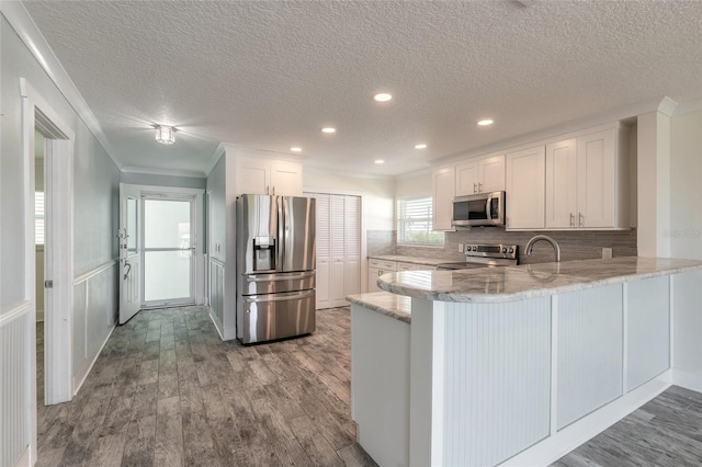 kitchen with wood finished floors, stainless steel appliances, a peninsula, white cabinets, and light stone countertops