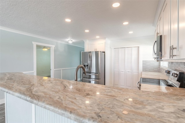 kitchen with backsplash, crown molding, light stone counters, appliances with stainless steel finishes, and white cabinetry