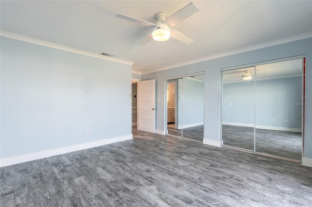 unfurnished bedroom with a textured ceiling, crown molding, multiple closets, and wood finished floors