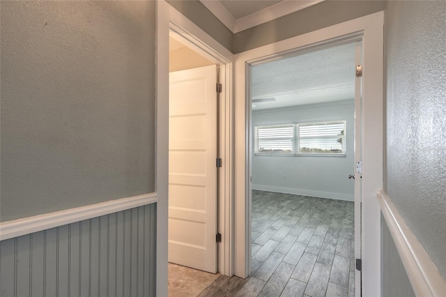 hall featuring a textured wall, a wainscoted wall, a textured ceiling, and light wood finished floors