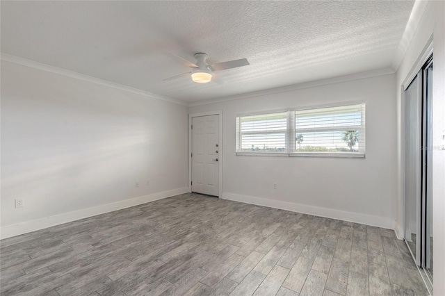 interior space featuring crown molding, baseboards, light wood-type flooring, a textured ceiling, and a ceiling fan