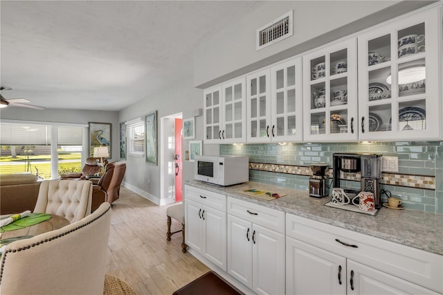 kitchen with visible vents, open floor plan, white cabinets, decorative backsplash, and white microwave