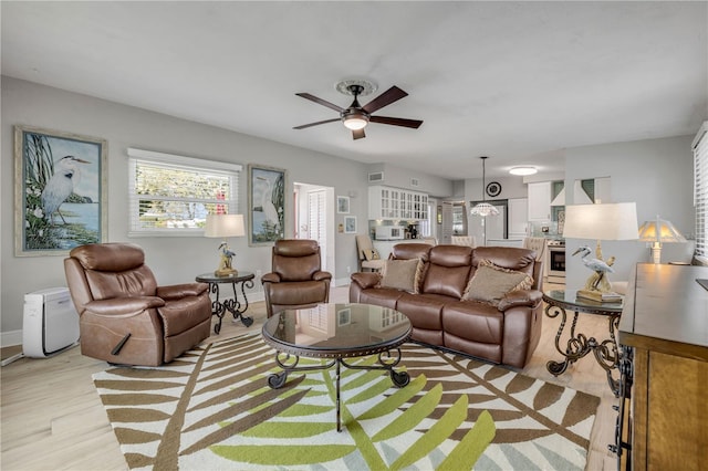 living room featuring a ceiling fan, light wood-style floors, visible vents, and baseboards