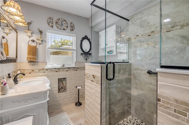 bathroom featuring vanity, tile walls, a stall shower, and wainscoting