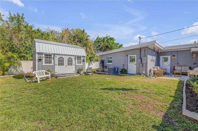 rear view of house featuring central air condition unit, an outbuilding, a lawn, an outdoor living space, and a fenced backyard