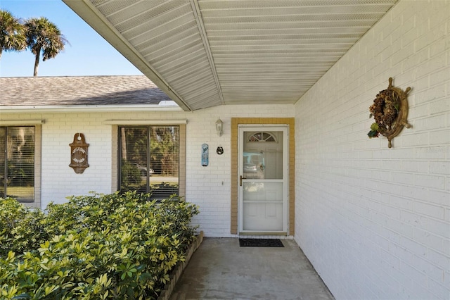 property entrance featuring brick siding and a shingled roof