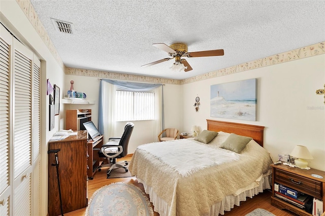 bedroom with a ceiling fan, wood finished floors, visible vents, a closet, and a textured ceiling