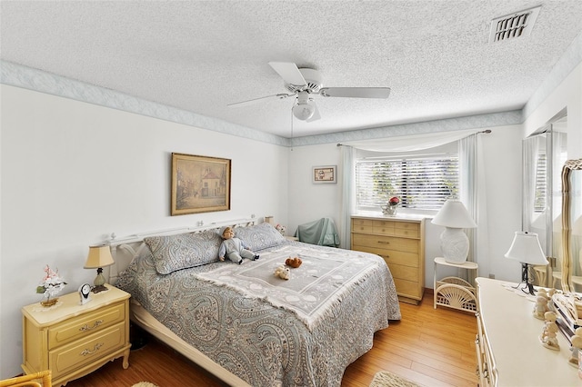 bedroom with light wood-type flooring, visible vents, a textured ceiling, and ceiling fan