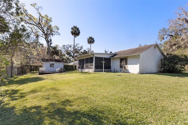 rear view of property with fence, a sunroom, an outdoor structure, a storage unit, and a lawn