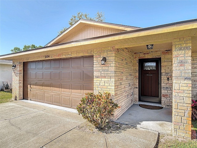 property entrance with a garage, brick siding, and concrete driveway