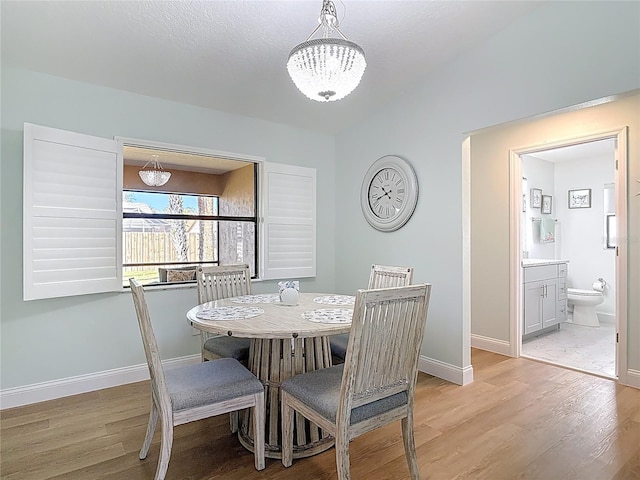 dining space featuring a chandelier, light wood-style flooring, baseboards, and vaulted ceiling