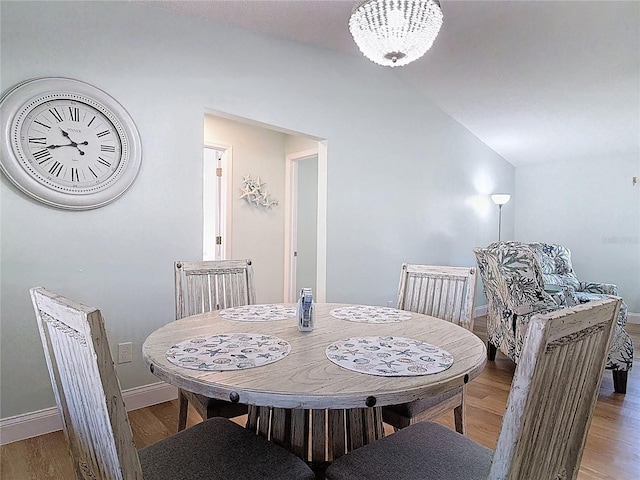 dining space featuring baseboards, lofted ceiling, wood finished floors, and a chandelier