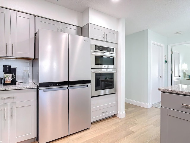 kitchen featuring gray cabinets, backsplash, stainless steel appliances, light wood finished floors, and light stone countertops