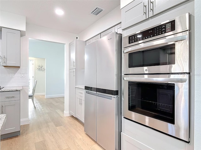 kitchen with visible vents, backsplash, appliances with stainless steel finishes, light wood finished floors, and baseboards