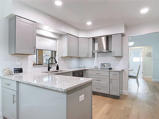 kitchen featuring light wood finished floors, a sink, decorative backsplash, gray cabinetry, and wall chimney exhaust hood