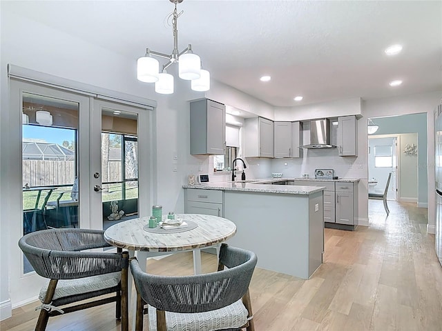 kitchen with wall chimney range hood, french doors, gray cabinets, and light wood-style flooring