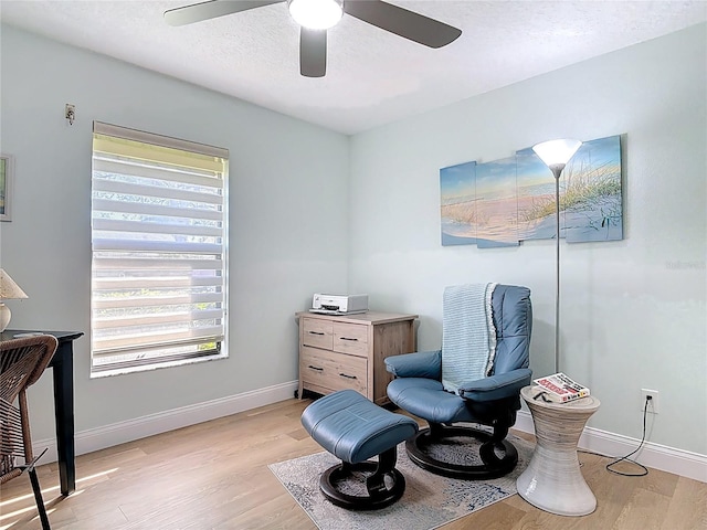 living area featuring a ceiling fan, baseboards, light wood-type flooring, and a textured ceiling