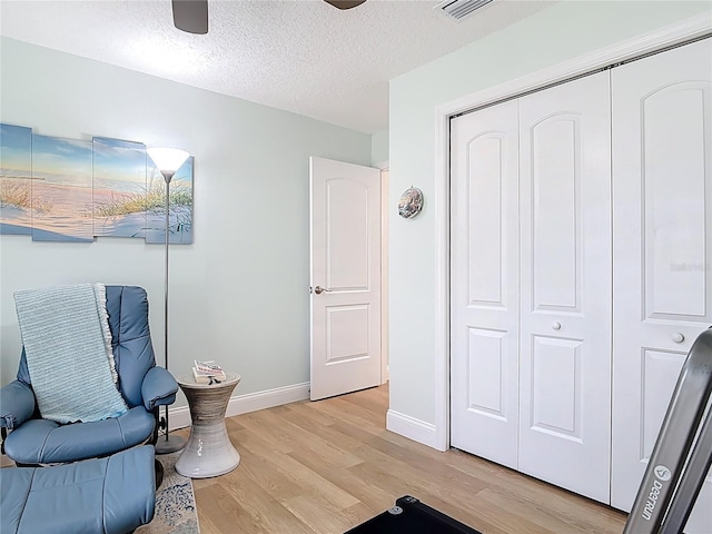 living area with visible vents, baseboards, a textured ceiling, and light wood-style flooring