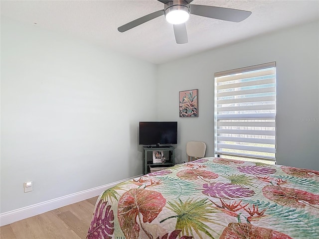 bedroom with light wood-style flooring, a textured ceiling, baseboards, and a ceiling fan