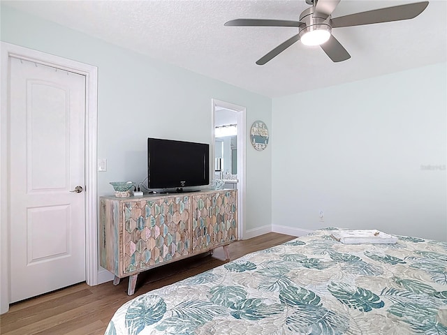 bedroom with ceiling fan, wood finished floors, baseboards, and a textured ceiling