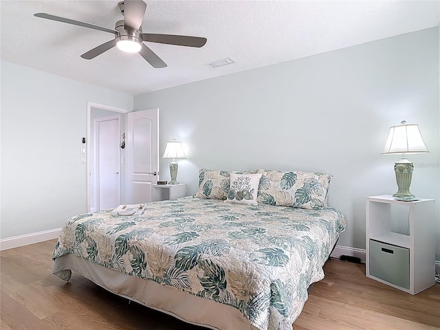 bedroom featuring visible vents, a ceiling fan, baseboards, and wood finished floors