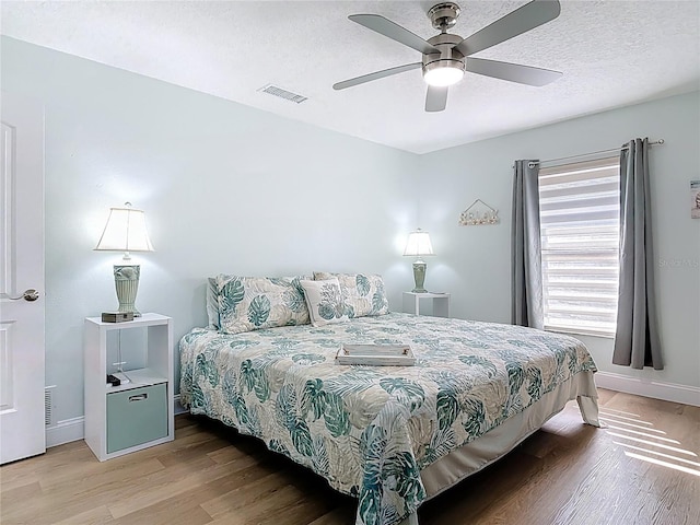 bedroom featuring visible vents, ceiling fan, baseboards, wood finished floors, and a textured ceiling