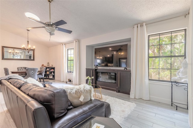 living area featuring ceiling fan with notable chandelier, a textured ceiling, a glass covered fireplace, and vaulted ceiling