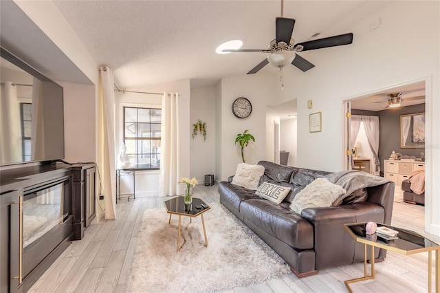 living room featuring lofted ceiling, a textured ceiling, ceiling fan, and light wood finished floors