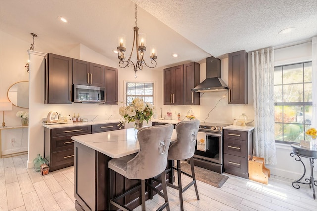 kitchen with light countertops, light wood-style floors, a notable chandelier, stainless steel appliances, and wall chimney exhaust hood