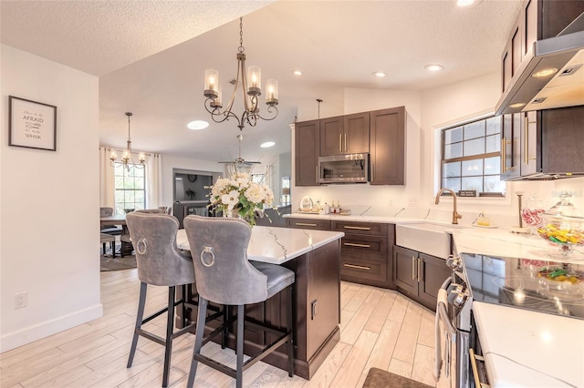 kitchen with light stone countertops, light wood-style flooring, a notable chandelier, stainless steel appliances, and a sink