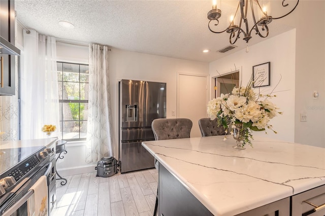 dining area featuring a chandelier, visible vents, a textured ceiling, and light wood-style floors