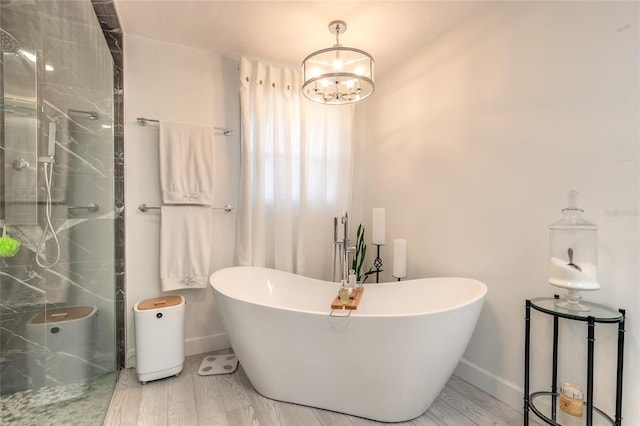 bathroom with a shower stall, baseboards, a chandelier, a freestanding bath, and wood finished floors